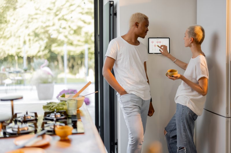 girl choosing temperature on thermostat of smart home system while her black boyfriend looking at her.