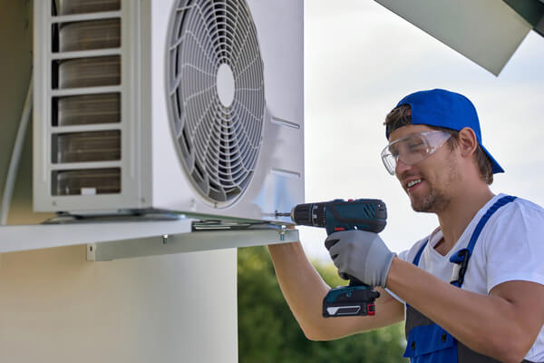 worker installs the outer metal case of the air conditioner with a drill